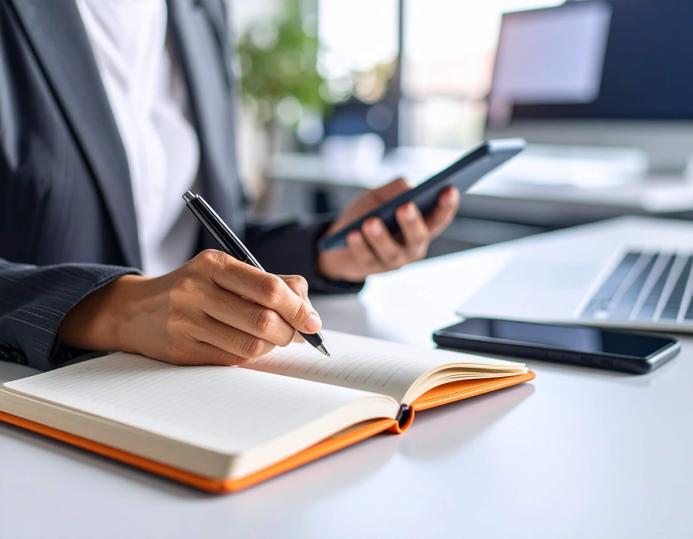 A person writing ecommerce audit and insight notes in a notebook whilst looking at a mobile phone