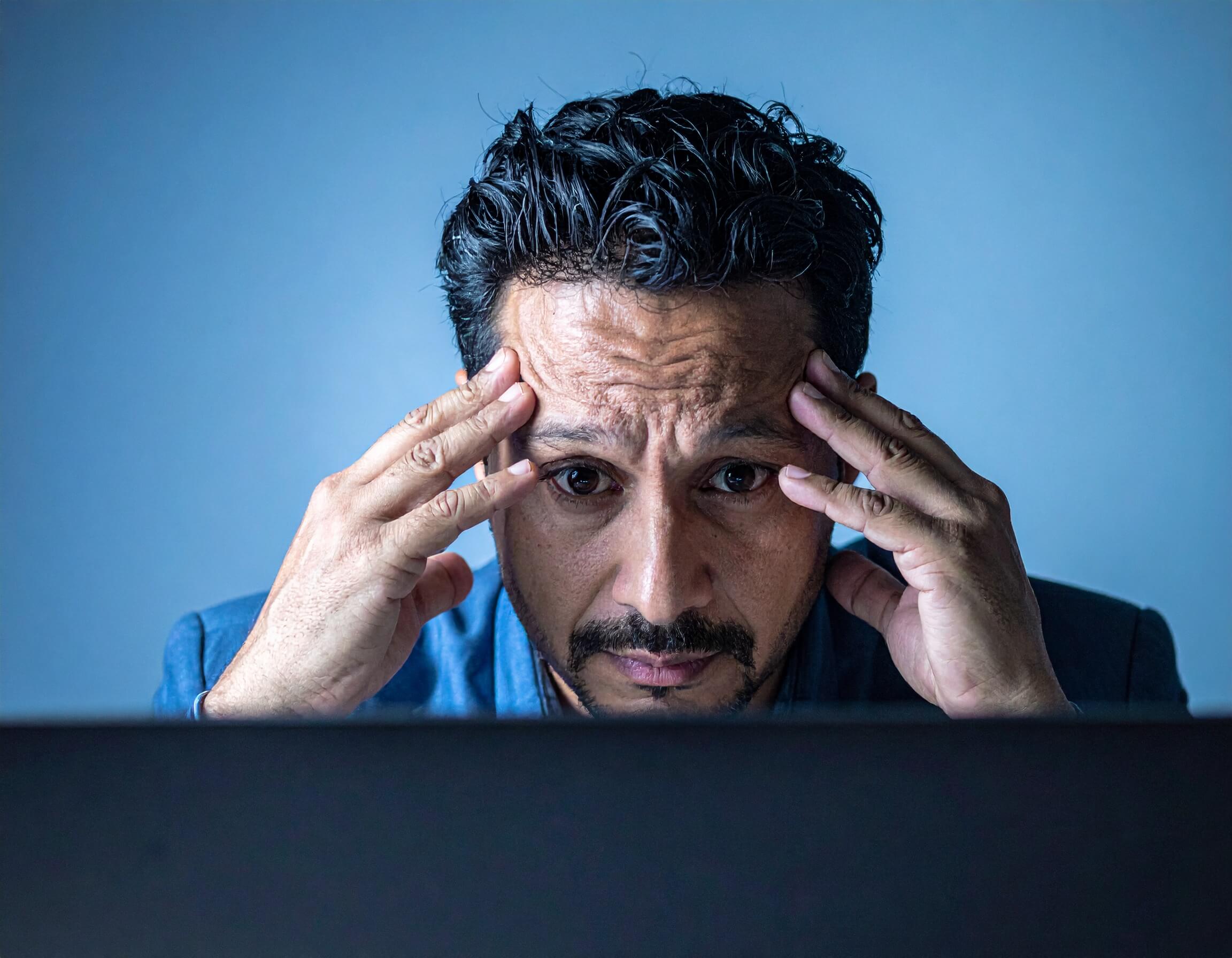 A man, head in hands, staring at a computer screen, worried about conversion killers on ecommerce sites